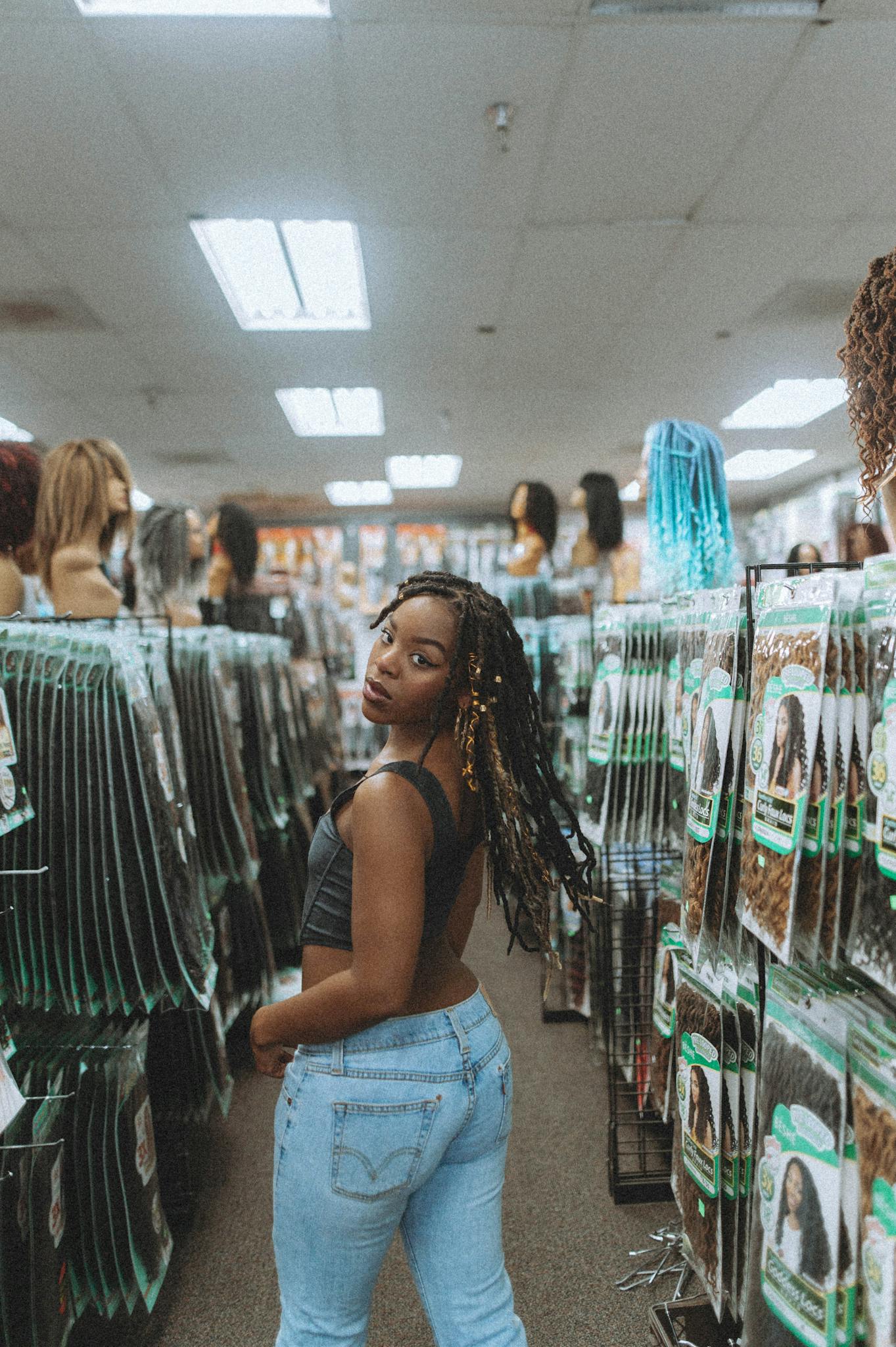 African American woman in denim and tank top looking back in a wig shop.