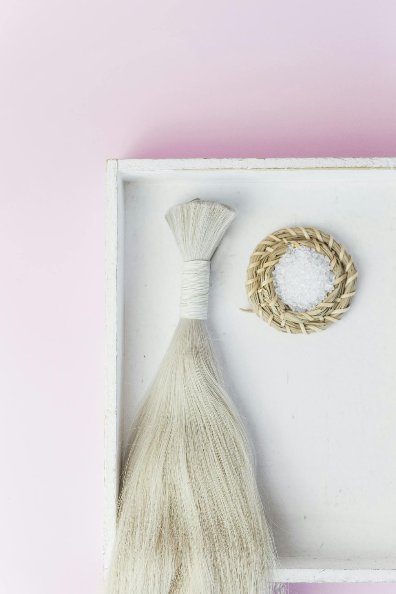 Blonde hair extension placed on a tray with a bright pink background.
